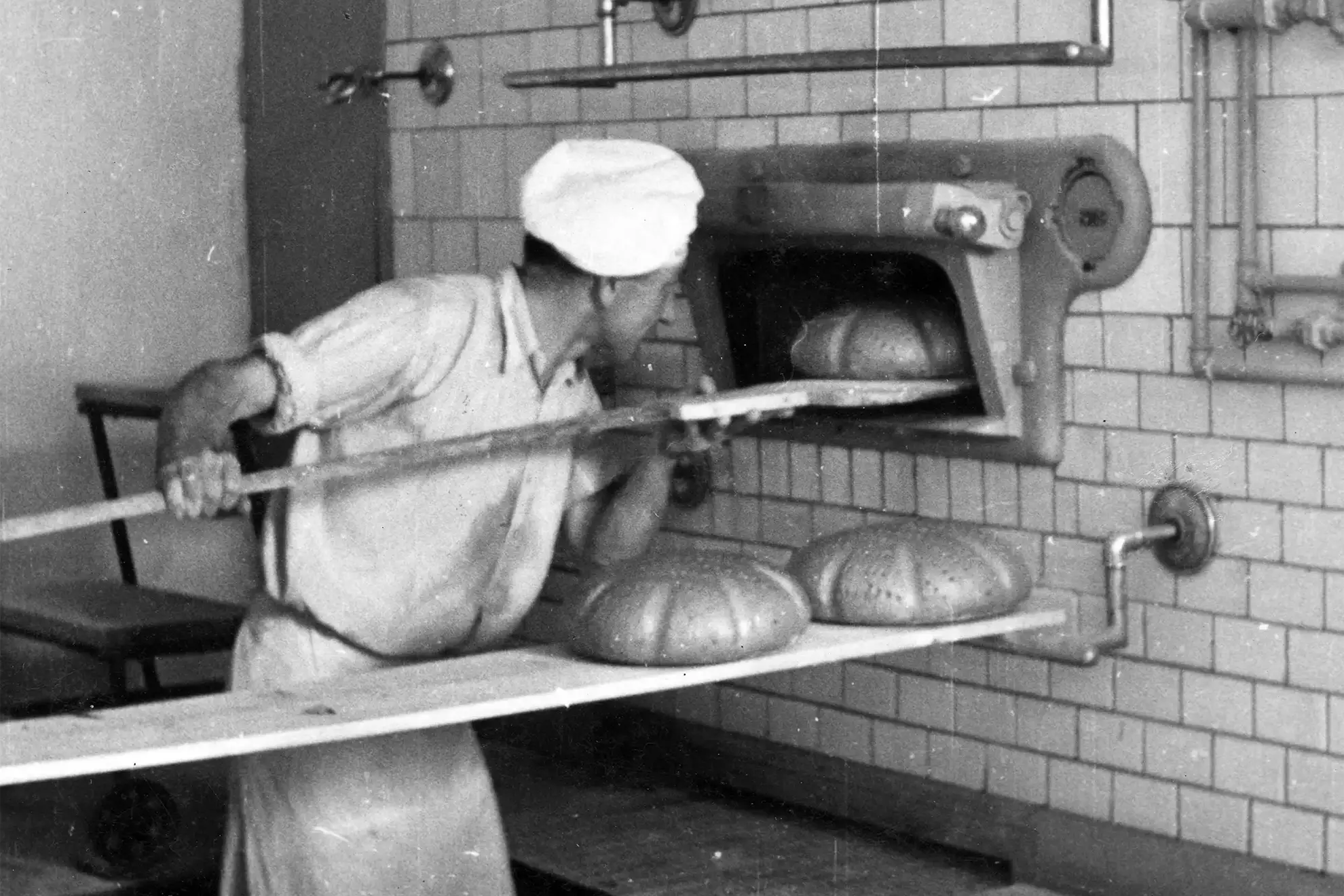 Der Großvater von Karl Wiesender schiebt auf einem schwarz-weiß Foto ein Brot in den Holzofen