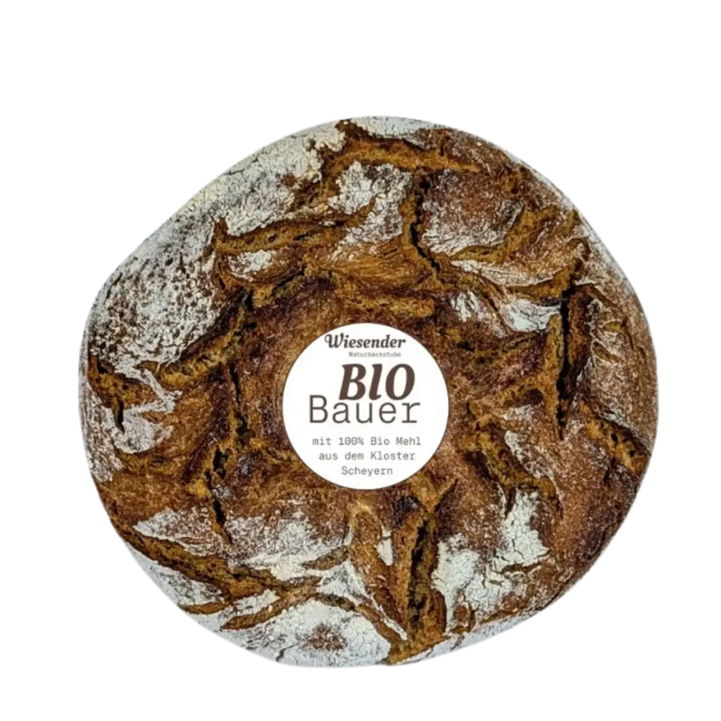 Ein runder, rustikaler Brotlaib mit rissiger, dunkler Kruste, bestäubt mit Mehl. In der Mitte befindet sich ein Etikett mit der Aufschrift "Bäckerei Wiesender BIO Bauer" aus Freising, das darauf hinweist, dass es mit Bio-Mehl aus der Naturbackstube hergestellt wurde.