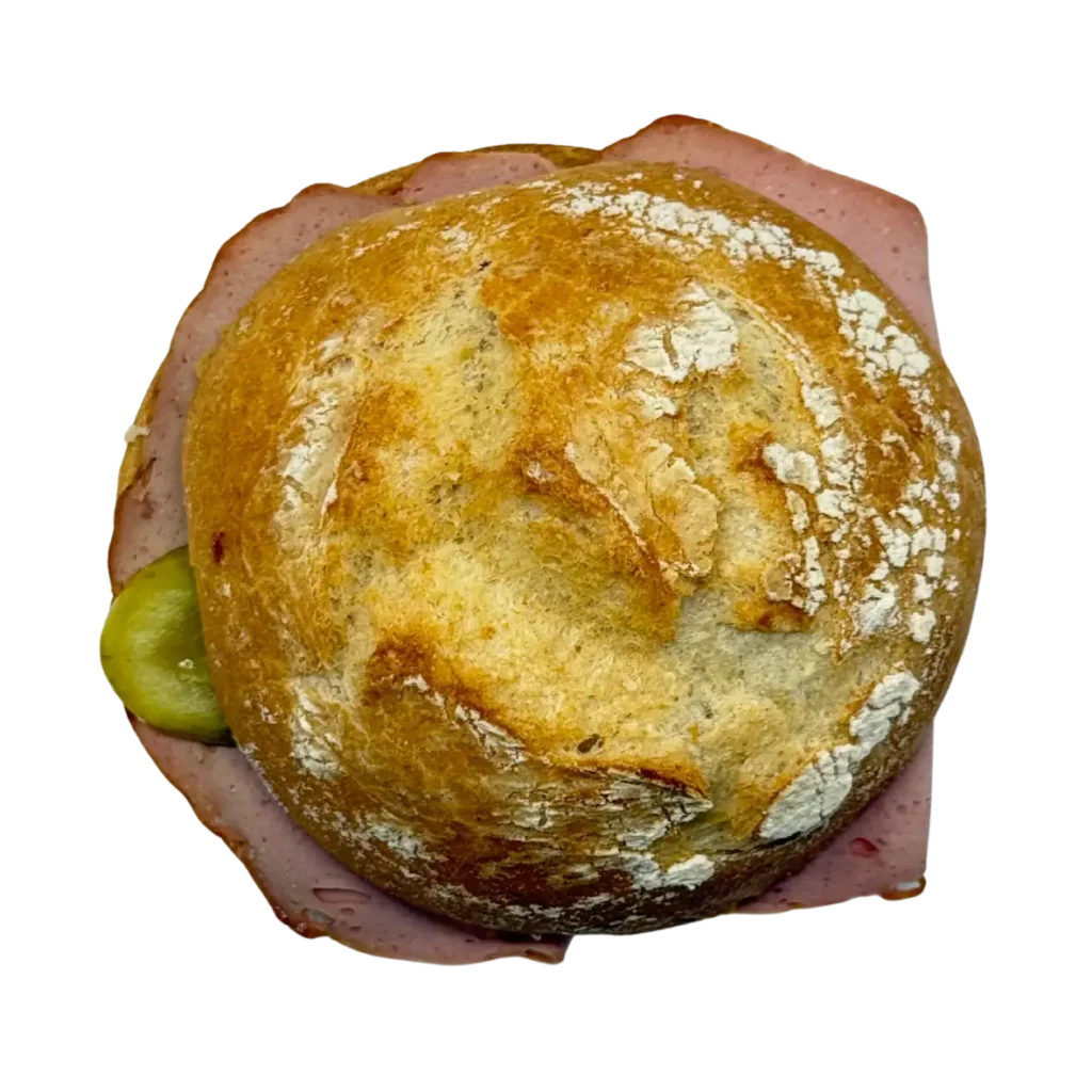 Ein rundes, knuspriges Brötchen der Bäckerei Wiesender in Freising, gefüllt mit Aufschnitt und einer Essiggurke, ist von oben auf weißem Hintergrund zu sehen.