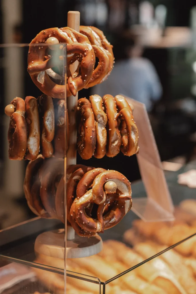 Ein Holzständer zeigt mehrere goldbraune Brezen mit sichtbaren Salzkristallen hinter einer Glastheke in der Bäckerei Wiesender.