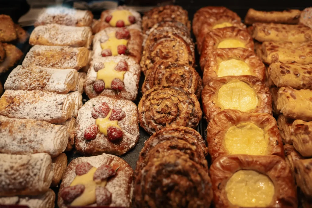 In Bäckerei Wiesnder ist eine Auswahl an Gebäck ordentlich in Reihen angeordnet, darunter mit Früchten belegte Törtchen oder Nussschnecken.