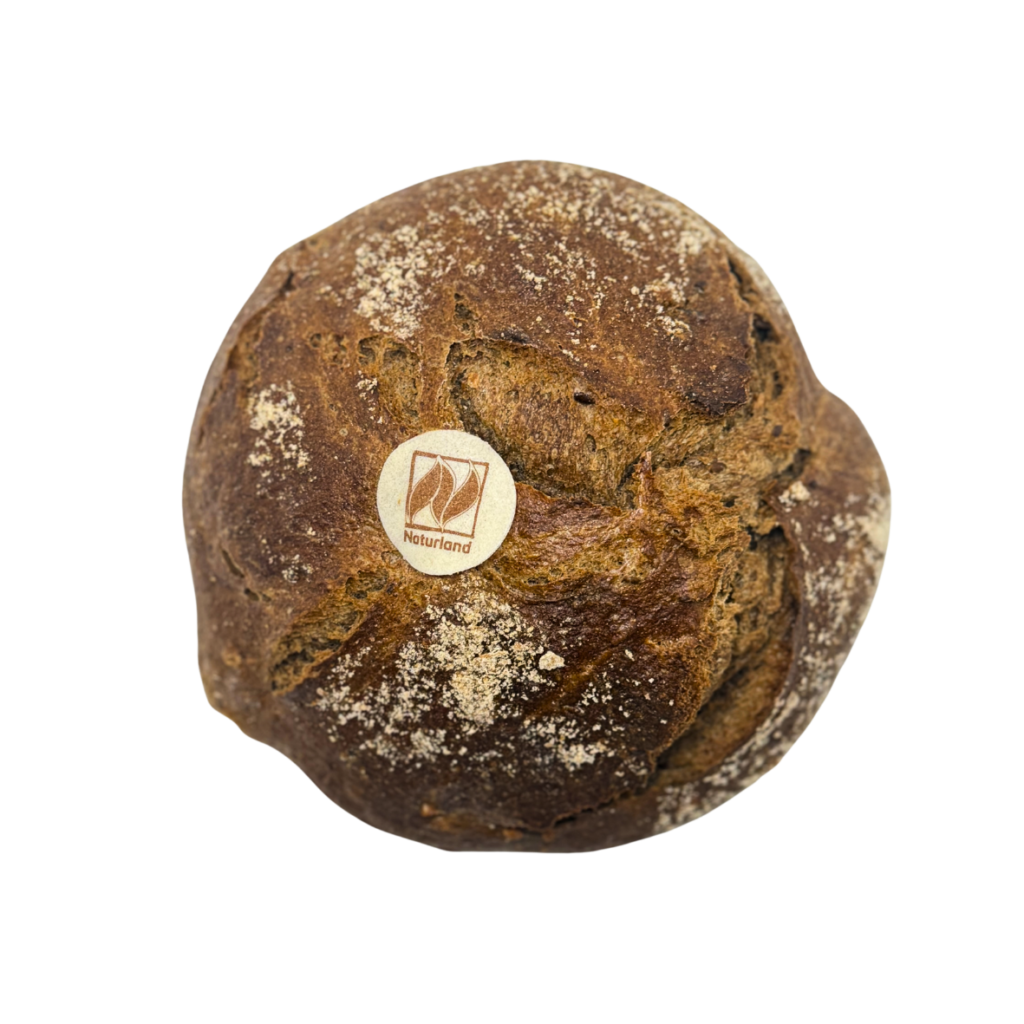 Ein runder Laib dunkles, rustikales Brot aus der Naturbackstube Wiesender in Moosburg, mit einer knusprigen, mit Weißmehl bestäubten Oberfläche, die tiefe Risse und eine dichte Textur aufweist.