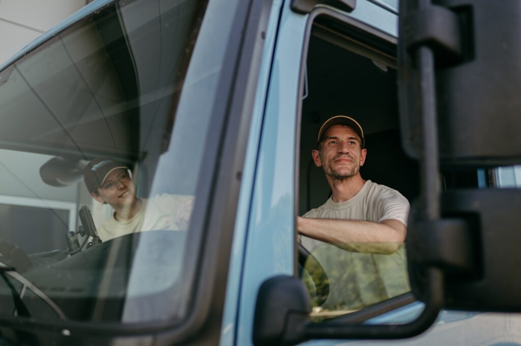 zwei FahrerInnen sitzen in einem blauen Wiesender LKW und schauen raus